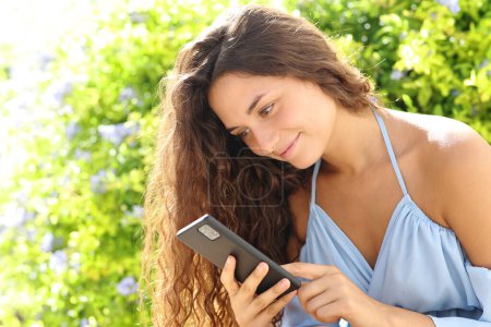 Téléchargez les photos : Femme heureuse utilisant un téléphone portable assis dans un parc - en image libre de droit