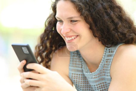Téléchargez les photos : Femme heureuse utilisant téléphone intelligent souriant à l'extérieur - en image libre de droit