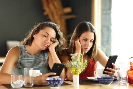 Foto de Amigos aburridos revisando teléfonos inteligentes en un restaurante - Imagen libre de derechos
