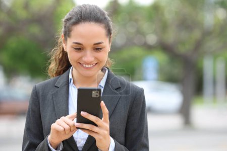 Téléchargez les photos : Portrait en première vue d'une femme d'affaires heureuse utilisant un téléphone portable marchant dans la rue - en image libre de droit