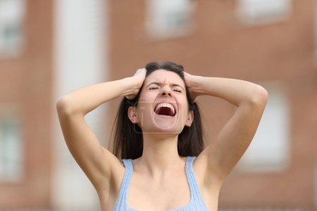Desperate woman yelling with hands on head in the street
