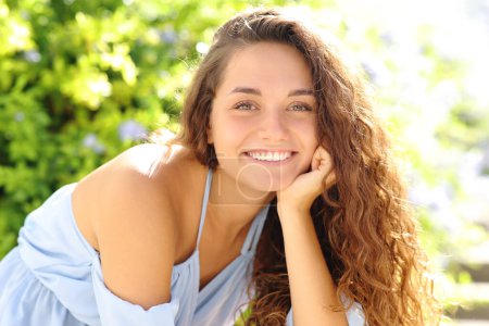 Téléchargez les photos : Joyeux beauté femme souriant à la caméra avec des dents parfaites assis dans un parc - en image libre de droit