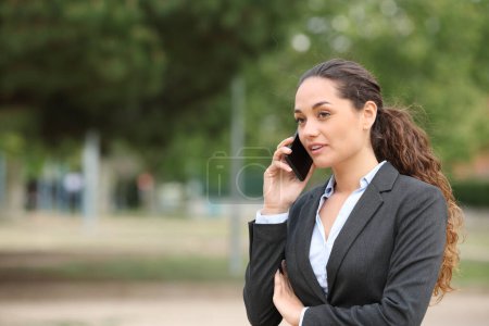 Photo for Businesswoman talking on mobile phone walking in a park - Royalty Free Image
