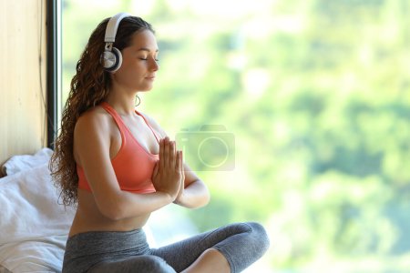 Foto de Yogi with headphones listening yoga audio guide at home near a window - Imagen libre de derechos