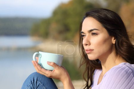 Photo for Serious woman drinking coffee looking away sitting in nature - Royalty Free Image