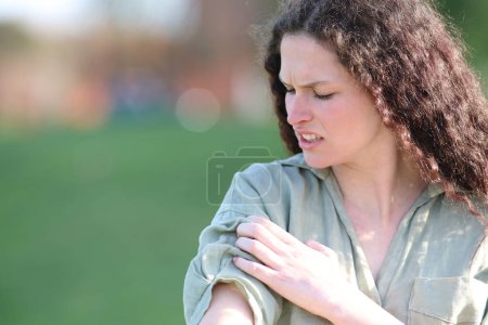 Téléchargez les photos : Woman complaining scratching itchy arm in a park - en image libre de droit