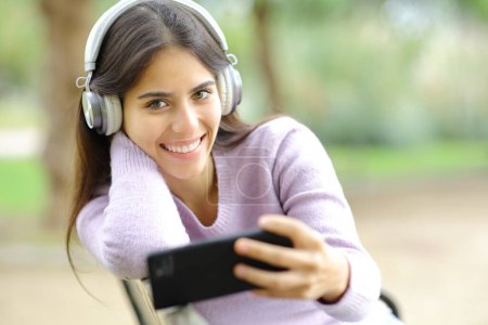 Téléchargez les photos : Happy woman listening to music looking at you in a park - en image libre de droit