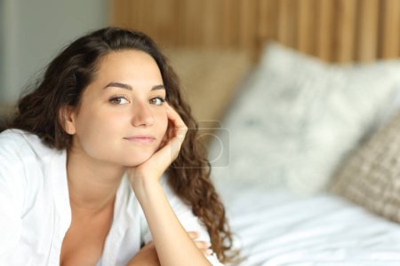 Photo for Relaxed woman looking at camera lying on the bed in a bedroom - Royalty Free Image