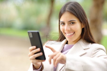 Téléchargez les photos : Woman in winter looks at you holding phone in a park - en image libre de droit