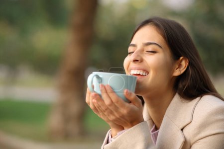 Téléchargez les photos : Happy woman in winter enjoying coffee laughing in a park - en image libre de droit