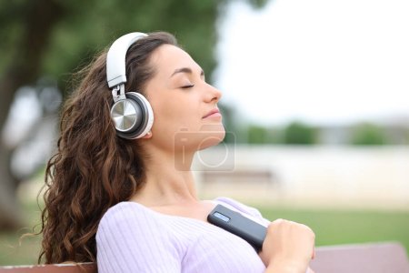 Photo for Relaxed woman resting in a bench listening music - Royalty Free Image