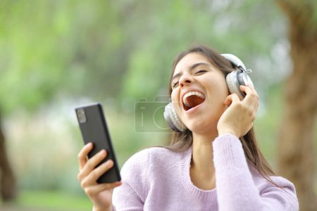 Photo for Happy teen singing in a park listening music with headphones and phone - Royalty Free Image