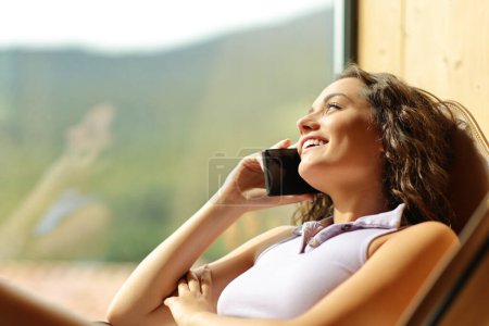 Foto de Happy woman on a chair talking on phone smiling - Imagen libre de derechos