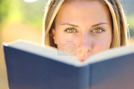 Téléchargez les photos : Vue de face d'une belle femme lisant un livre vous regardant avec des yeux étonnants - en image libre de droit