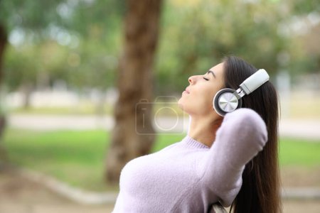Foto de Retrato de una mujer descansando escuchando música en un banco de un parque - Imagen libre de derechos