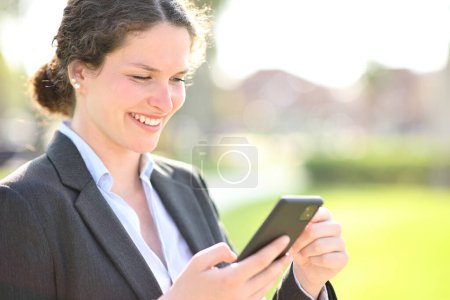 Photo for Businesswoman checking smart phone in a park - Royalty Free Image