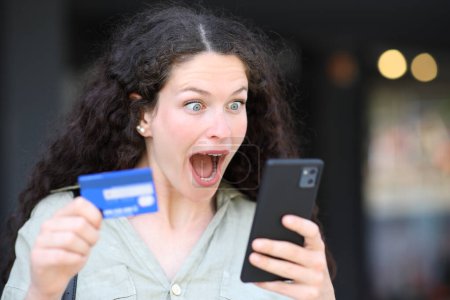 Téléchargez les photos : Femme surprise achetant en ligne avec téléphone et carte de crédit - en image libre de droit