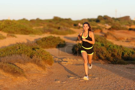Téléchargez les photos : Front vie wof a runner woman running in the mountain towards camera at sunset - en image libre de droit