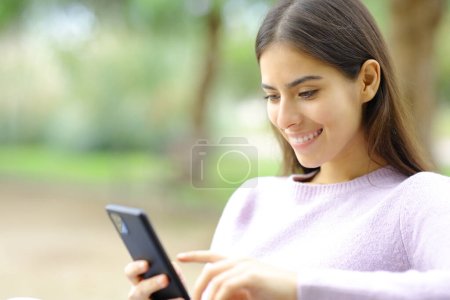 Photo for Happy woman checking cell phone in a park - Royalty Free Image