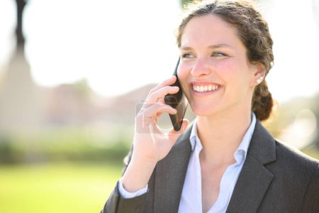 Photo for Happy businesswoman using cell phone smiling in a park - Royalty Free Image