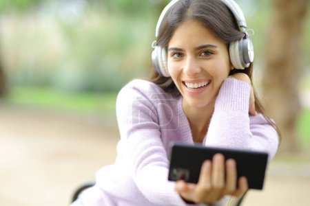 Foto de Mujer feliz te mira escuchando música en un parque - Imagen libre de derechos
