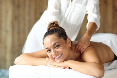 Happy woman receiving massage looking at camera in spa