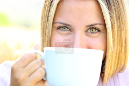 Téléchargez les photos : Vue de face gros plan d'un adolescent heureux avec des yeux de beauté tenant tasse de café en regardant la caméra - en image libre de droit