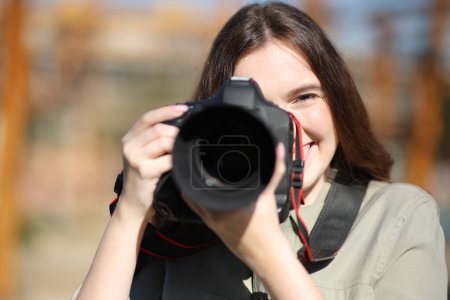 Front view portrait of a happy photographer taking photos with dslr professional camera