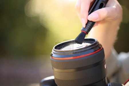 Téléchargez les photos : Portrait rapproché d'un photographe nettoyant l'objectif de la caméra avec une brosse à l'extérieur - en image libre de droit