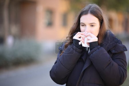 Foto de Mujer enferma usando tejido para limpiar la nariz en la calle en invierno - Imagen libre de derechos