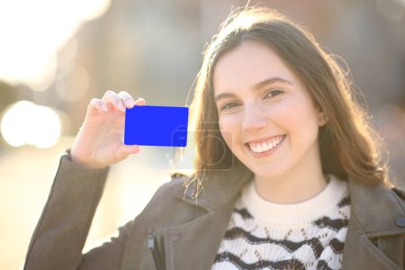 Téléchargez les photos : Femme heureuse montrant la carte de crédit à la caméra dans la rue au coucher du soleil - en image libre de droit