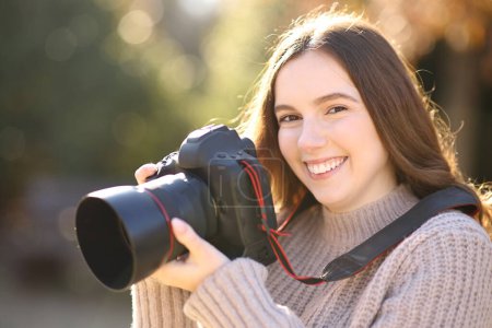 Téléchargez les photos : Heureux photographe tenant dslr caméra vous regarde dans un parc - en image libre de droit