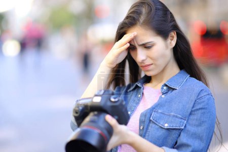 Téléchargez les photos : Photographe inquiet vérifiant les résultats des séances photo sur l'appareil photo dans la rue - en image libre de droit