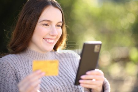 Photo for Happy woman buying online with phone and credit card in a park - Royalty Free Image
