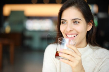 Téléchargez les photos : Femme heureuse buvant du soda dans un restaurant regardant loin dans un restaurant - en image libre de droit