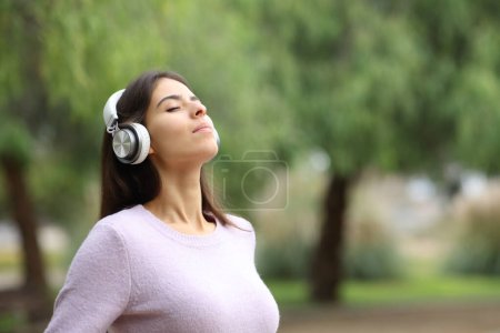 Téléchargez les photos : Femme détendue respirant de l'air frais avec casque méditant dans un parc - en image libre de droit