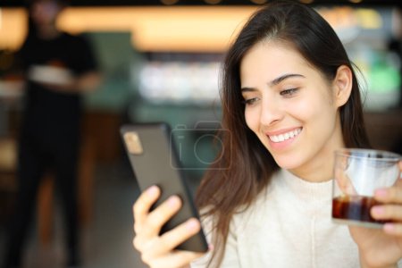Téléchargez les photos : Heureux client vérifiant téléphone portable tenant soda dans un restaurant - en image libre de droit