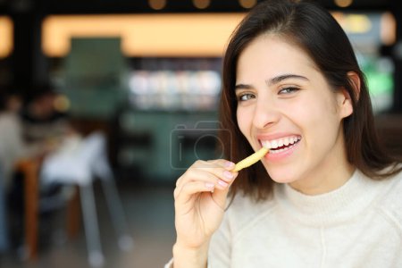 Foto de Mujer feliz comiendo papas fritas mirando la cámara en un restaurante - Imagen libre de derechos