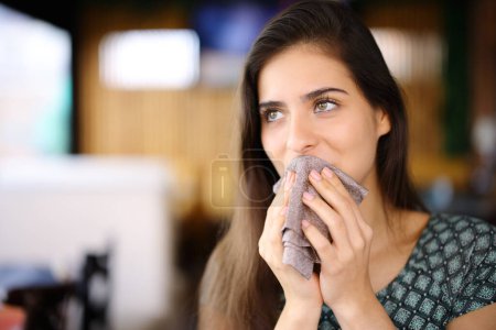 Téléchargez les photos : Femme nettoyage bouche avec serviette assis dans un restaurant regardant loin - en image libre de droit