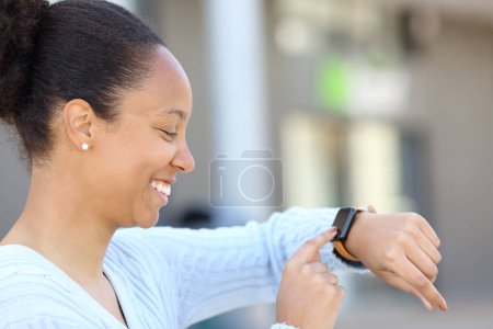 Photo for Profile of a happy black woman checking smartwatch in the street - Royalty Free Image