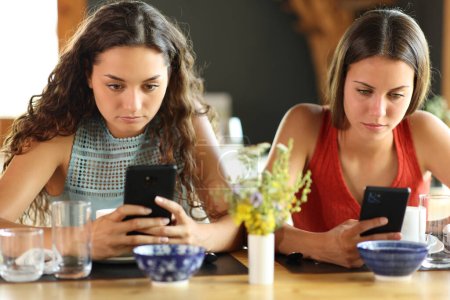 Téléchargez les photos : Vue de face de deux amis dans un restaurant qui s'ignorent en utilisant leur téléphone - en image libre de droit