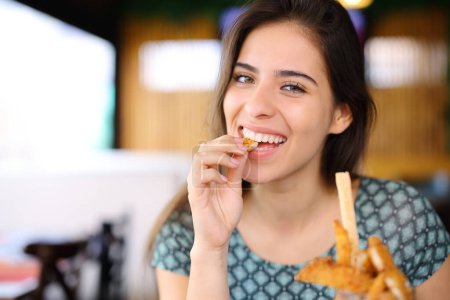 Foto de Mujer feliz comiendo dedos de pollo mirando la cámara en un restaurante - Imagen libre de derechos