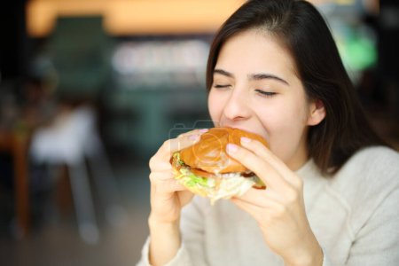 Foto de Mujer feliz comiendo hamburguesa en un restaurante - Imagen libre de derechos
