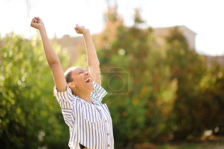 Foto de Mujer negra emocionada levantando brazos y gritando en un parque - Imagen libre de derechos