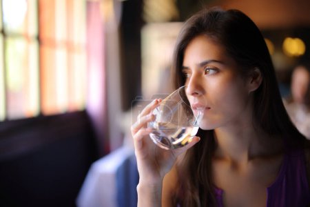 Foto de Mujer seria bebiendo agua sentada en un restaurante mirando a un lado - Imagen libre de derechos