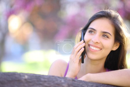 Téléchargez les photos : Vue de face portrait d'une belle femme heureuse appelant au téléphone au printemps dans un parc - en image libre de droit