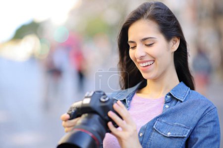 Téléchargez les photos : Joyeux photographe vérifiant les photos sur l'appareil photo dslr dans la rue - en image libre de droit