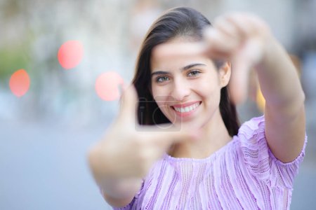 Téléchargez les photos : Vue de face portrait d'une femme heureuse encadrant avec les mains vous regardant dans la rue - en image libre de droit