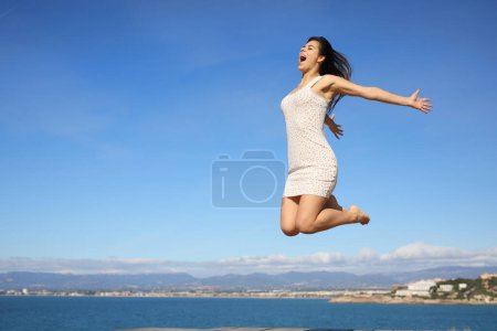 Foto de Mujer feliz saltando en la costa celebrando las vacaciones de verano - Imagen libre de derechos