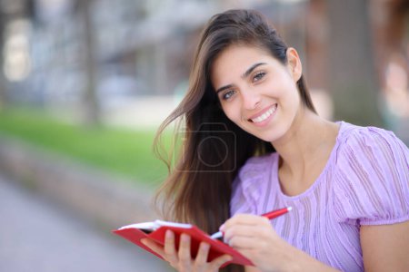 Foto de Mujer feliz escribiendo en agenda de papel te mira en la calle - Imagen libre de derechos